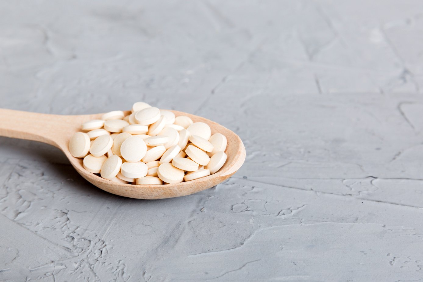 Heap of white pills on colored background. Tablets scattered on a table. Pile of red soft gelatin capsule. Vitamins and dietary supplements concept